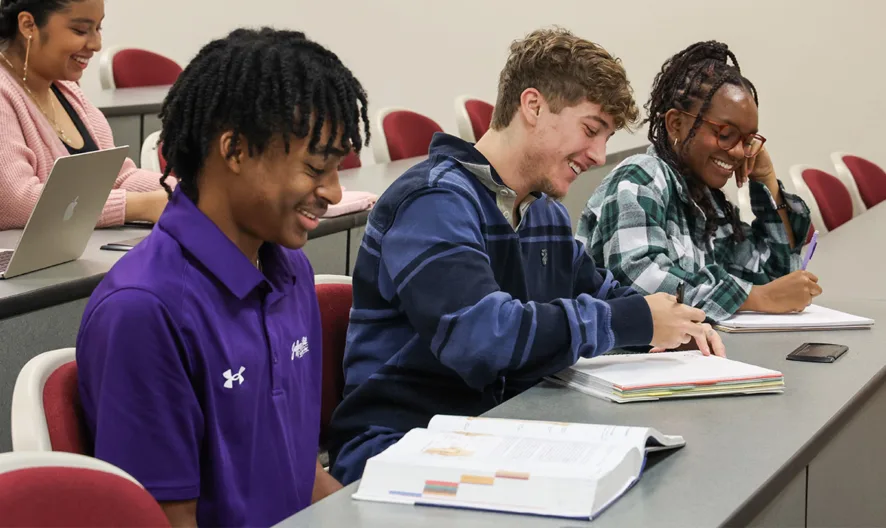 Students smiling while looking at textbooks in a classroom setting.
